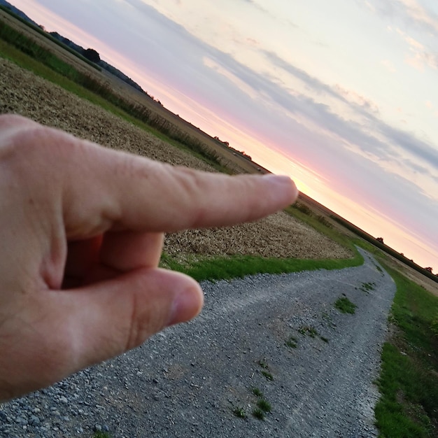 사진 해가 지는 동안 하늘을 배경으로 들판의 경로를 가리키는 손의 절단 이미지