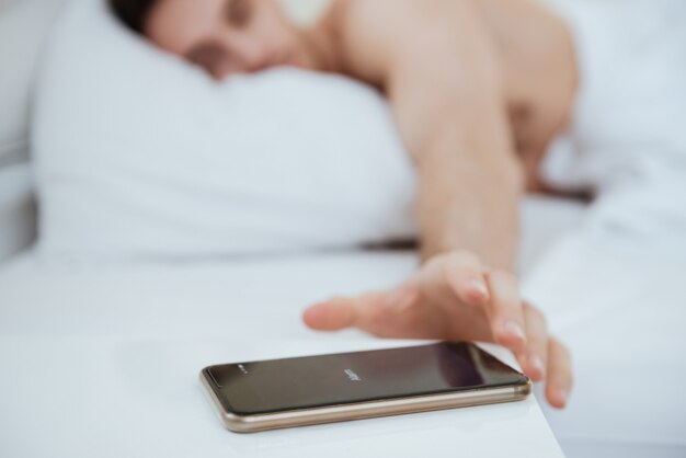 사진 침대에 누워 침대 근처에 있는 전화기를 잡아당기는 남자의 자른 이미지. 전화에 집중