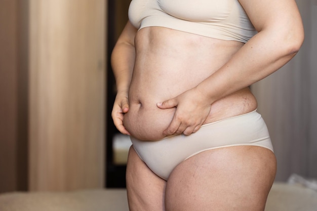 太りすぎの女性が下着にへそで脂肪を隠している大きな過剰な腹部を押し込んでいるトリミングされた画像おなかをぶら下げて腹部を引き離す