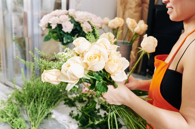 Фото Обрезанное изображение улыбающегося флориста, делающего красивый букет из белых роз и ромашек для невесты