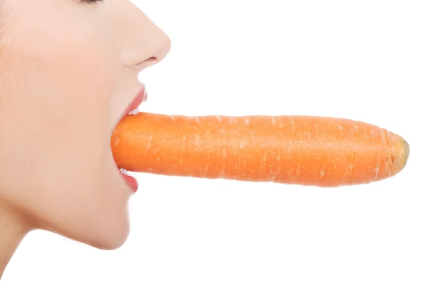 Фото Обрезанное изображение молодой женщины с морковью во рту на белом фоне