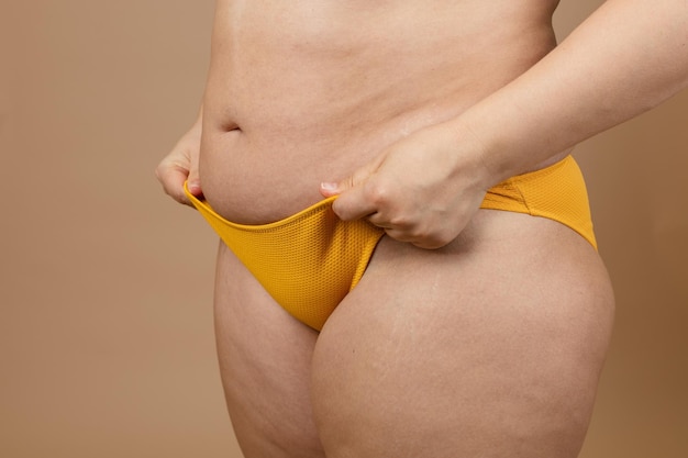 Photo cropped image of overweight woman tucking hiding fat naked big excessive belly in yellow pants dangling down stomach