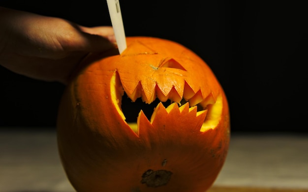 Photo cropped image of person carving pumpkin at table