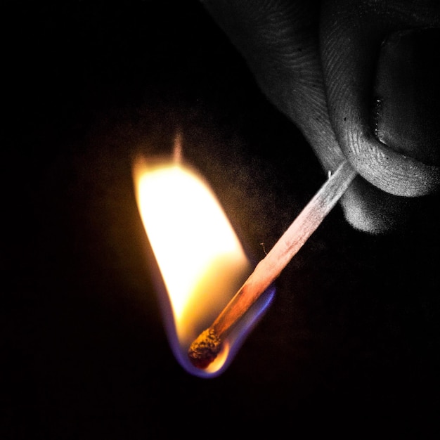 Photo cropped image of person holding burning matchstick against black background