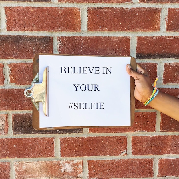 Photo cropped image of person holding clipboard with text against brick wall