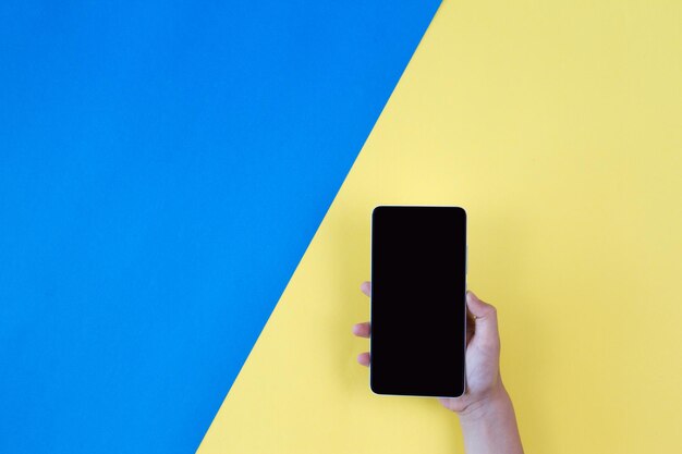 Cropped image of person holding smart phone against yellow and blue background