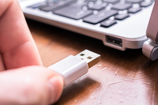 Cropped image of person holding usb cable by laptop at desk