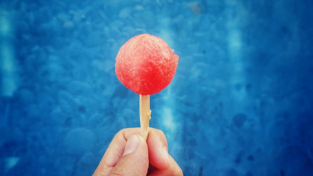 Photo cropped image of person holding watermelon lollipop