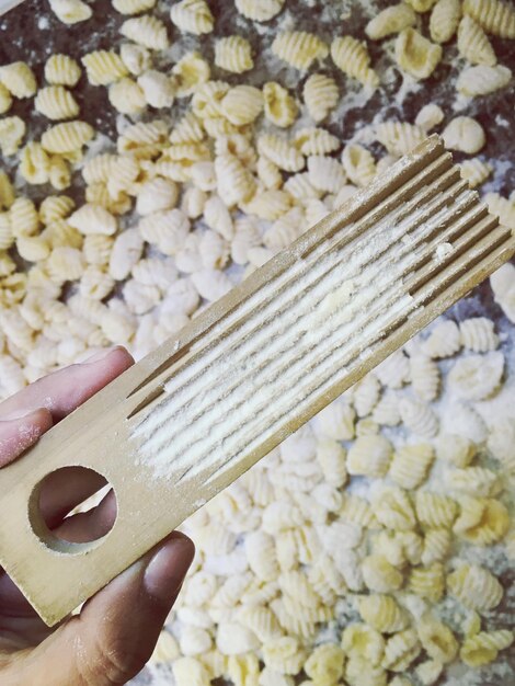 Cropped image of person holding wooden tool over gnocchi