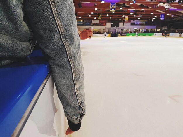 Cropped image of person sitting on seat by ice-rink