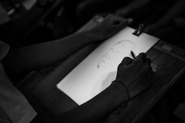 cropped image of person sketching on paper in darkroom