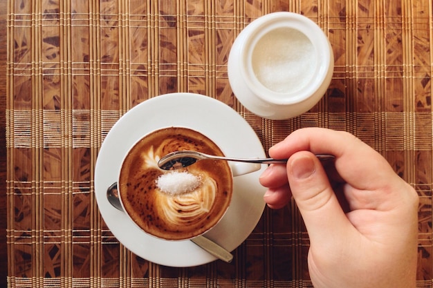 テーブルの上でスプーンでコーヒーを混ぜている人のカットされた画像