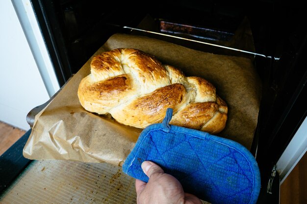 Photo cropped image of person taking braided bread from oven