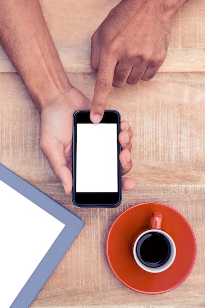 Cropped image of person using smart phone by coffee and tablet on table