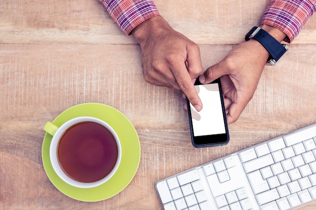Cropped image of person using smart phone on desk by coffee mug