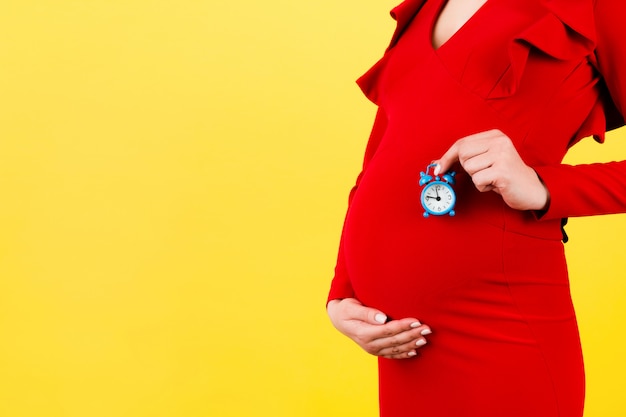 Cropped image of pregnant woman in red dress holding alarm clock