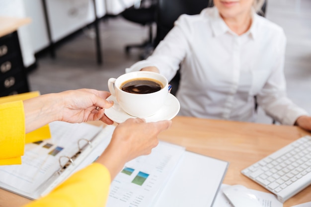 Photo cropped image of secretary bringing cup of coffee for her boss in office