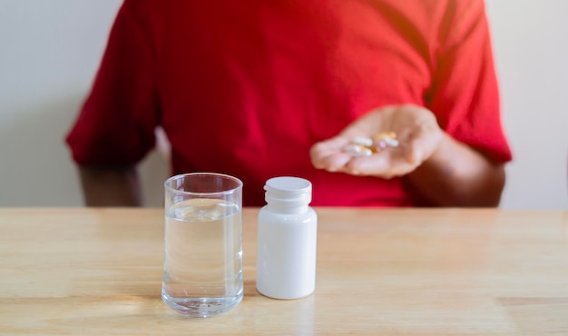 Cropped image of senior man in red TShirt taking medicine pill at home