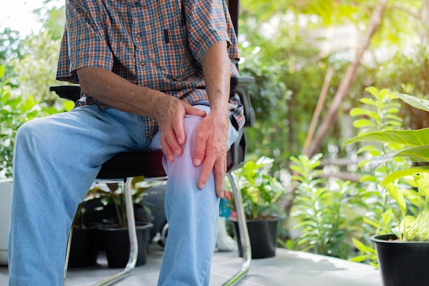 Photo cropped image of senior man sitting on chair in the garden and having knee pain
