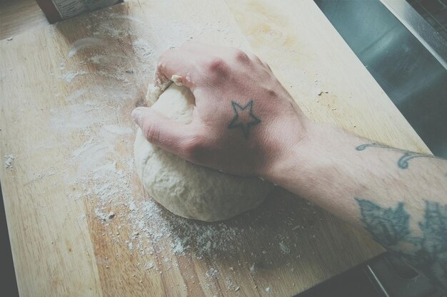 Photo cropped image of tattooed man hand kneading dough on table