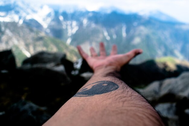 Photo cropped image of tattooed man hand reaching mountain