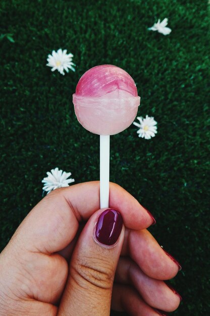 Foto immagine ritagliata di una donna con la mano che tiene un lecca-lecca rosa sul campo