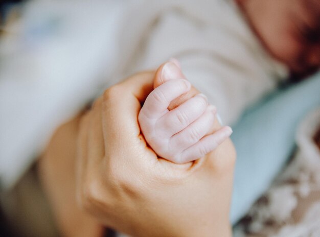 Photo cropped image of woman holding baby hand at home