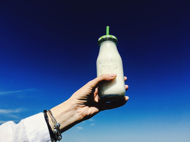 Cropped image of woman holding milk bottle against blue sky on sunny day