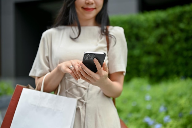 Cropped image of a woman is texting someone while walking on the street with her shopping bags