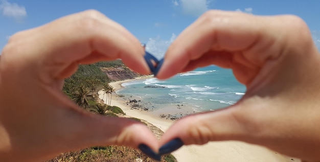 Foto immagine ritagliata di una donna che fa la forma di un cuore con le mani contro la spiaggia