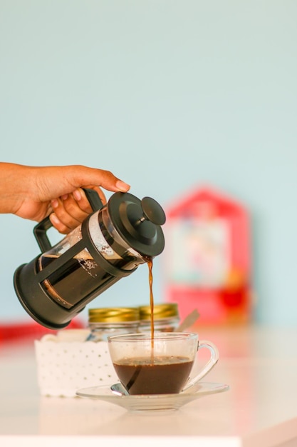 Photo cropped image of woman pouring coffee in cup from french press coffee maker on table