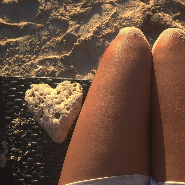 Foto immagine ritagliata di una donna seduta accanto a una pietra a forma di cuore su una panchina in spiaggia