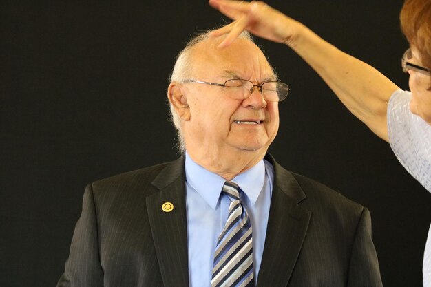 Cropped image of woman touching head of senior man against black background