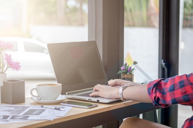 Cropped image of woman using laptop by coffee at cafe