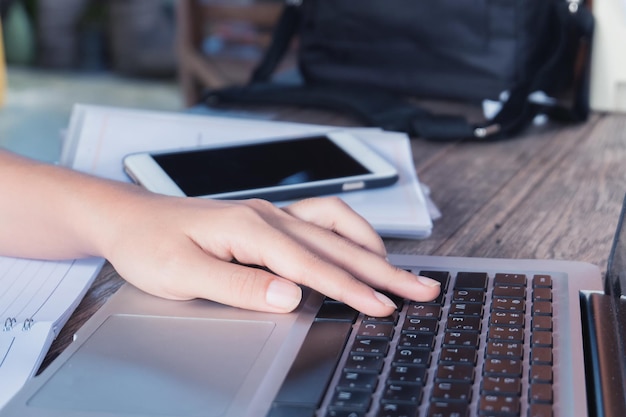 Cropped image of woman using laptop by smart phone at table