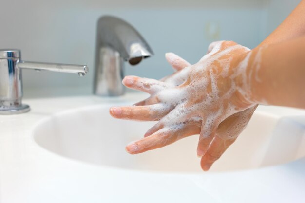 cropped image of woman washing hands in bathroom sink