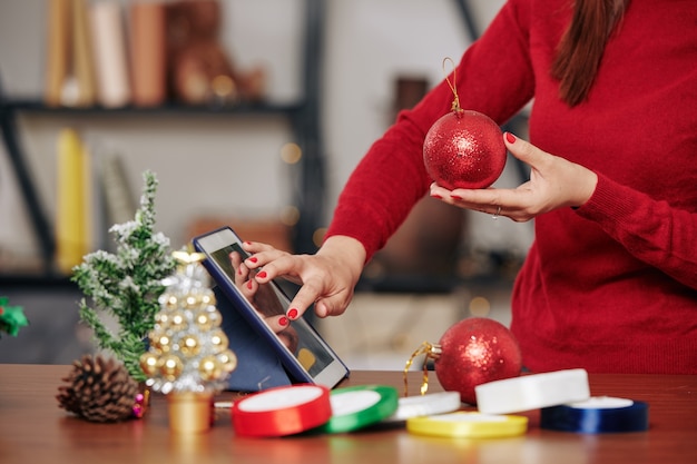 Cropped image of woman with big red bauble in hands ordering more Christmas decorations in online store