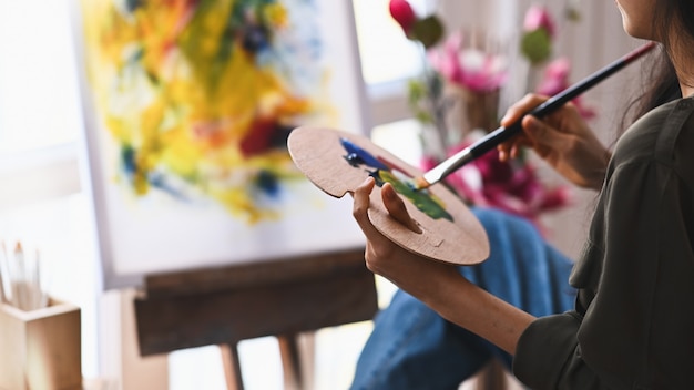 Cropped image of young artist girl holding a paint brush and drawing an oil colors on canvas