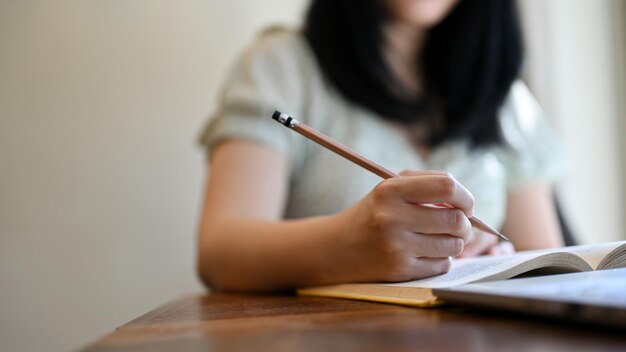 Cropped image A young Asian female college student doing homework writing on notebook