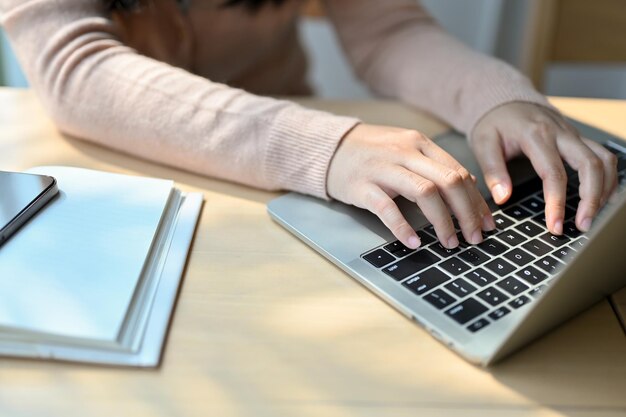 Cropped image of a young Asian female college student using a laptop typing on keyboard