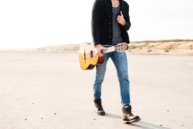 Cropped image of a young casual man walking with guitar at the seaside