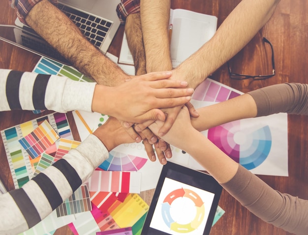 Cropped image of young designers holding hands together while working in office