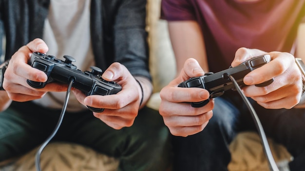 Photo cropped image of young men playing video games while sitting on sofa at home