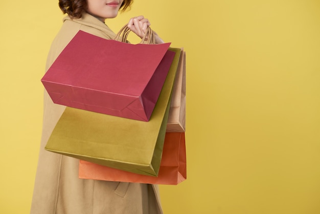 Cropped image of young woman holding many shopping bags and\
turning back to camera, isolated on yellow