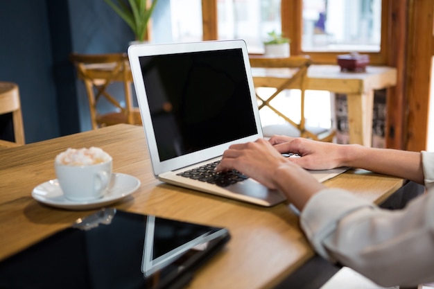 Cropped image of young woman using laptop at table in careteria