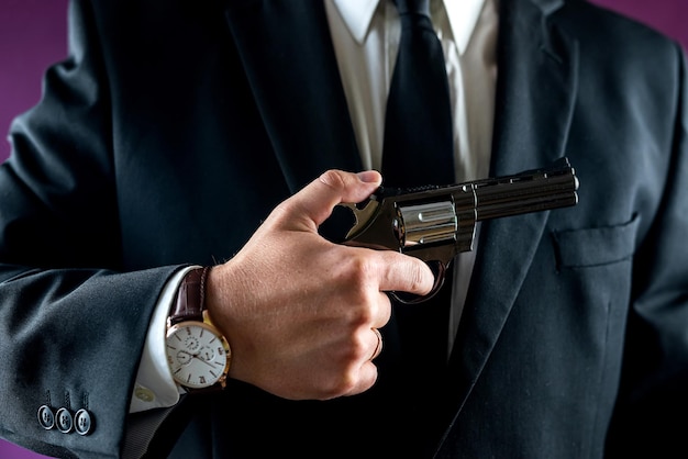 портрет человека в костюме, держащего пистолет, изолированный на простом фоне, револьвер в руках