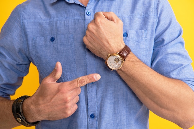 Uomo ritagliato che punta il dito a portata di mano guarda su sfondo giallo, tempo.