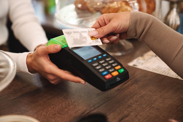 Donna matura ritagliata che paga la carta di credito al bar mentre il cameriere tiene in mano il terminale di pagamento