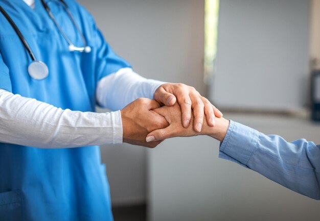 Cropped millennial male doctor in uniform calming shaking hand with old woman patient in clinic