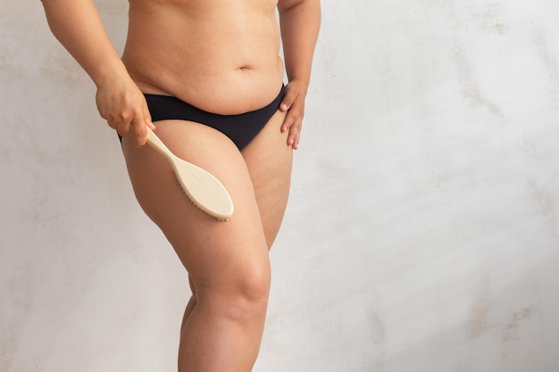 Femmina grassa sovrappeso ritagliata che sfrega strofinando le gambe dei fianchi in lingerie nera usando il massaggio secco della cellulite con spazzola